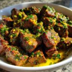 Close-up of tender crockpot steak cubes coated in a bright yellow, garlicky herb sauce.