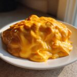 A generous mound of thick, bright orange nacho cheese sauce piled high on a small white plate, highlighted by sunlight.