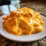 A thick, bright orange mound of creamy nacho cheese sauce sitting on a small white plate.
