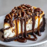 A rich slice of turtle cheesecake topped with pecans, dripping with chocolate and caramel sauce.