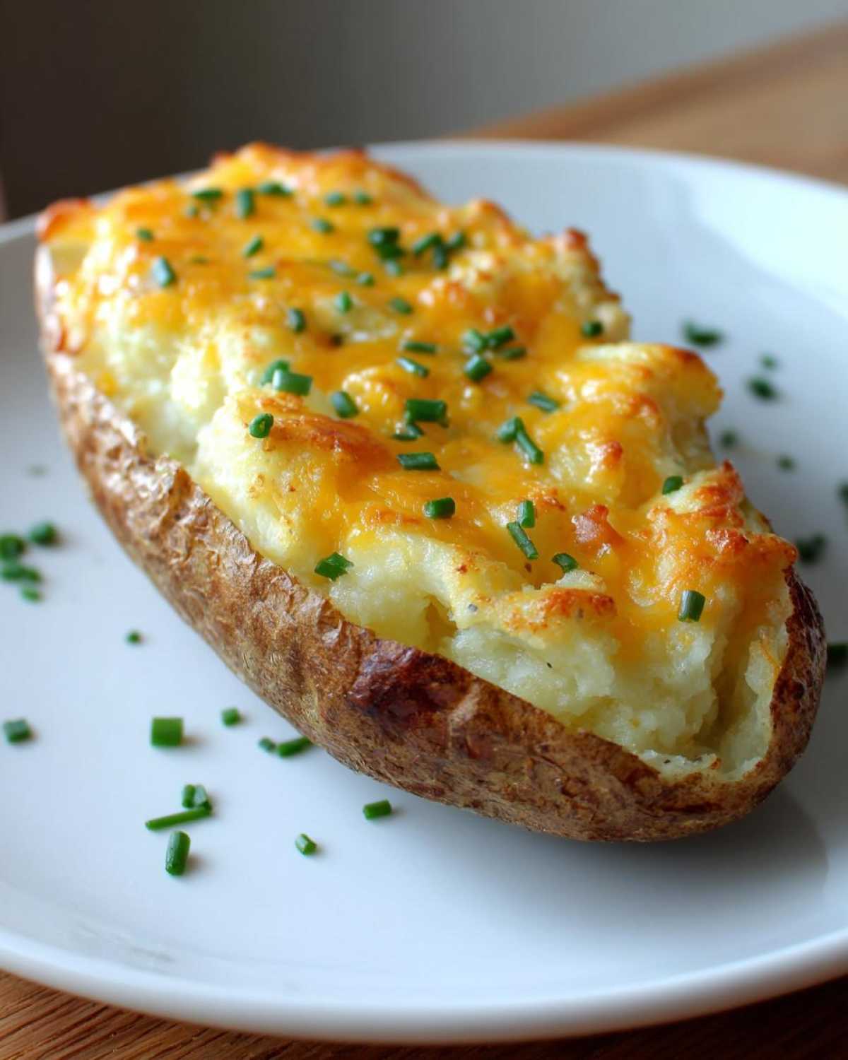 A close-up of a single twice baked potato stuffed with creamy filling, topped with melted cheddar cheese and fresh chives.