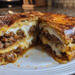 A cross-section view of the ultimate garbage bread, showing layers of seasoned ground meat and melted white cheese oozing out.