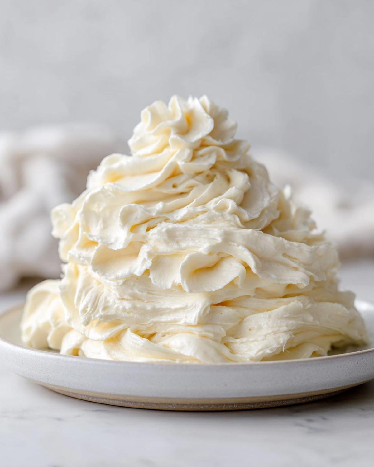 A large, beautifully piped mound of creamy vanilla buttercream frosting sitting on a small, light-colored plate.