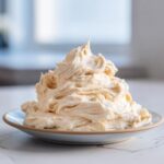 A generous mound of creamy, pale yellow vanilla buttercream frosting piped onto a small plate.