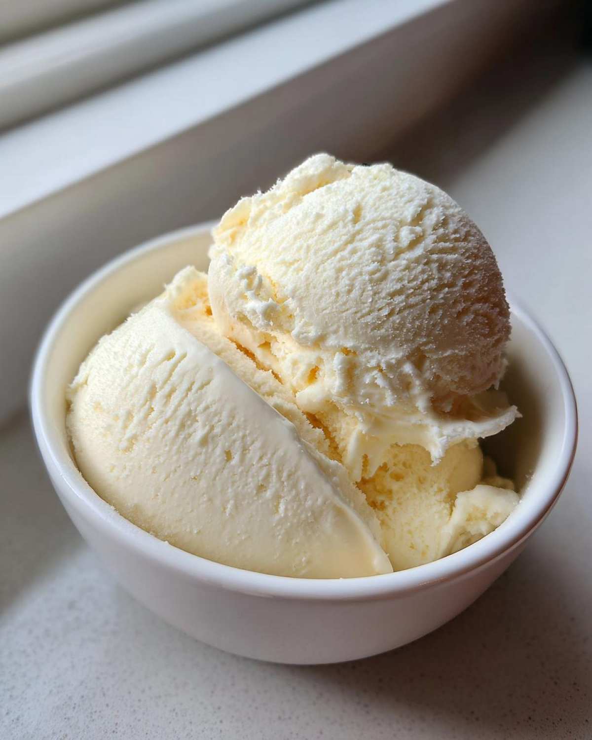 Close-up of creamy vanilla protein ice cream scoops served in a small white bowl.