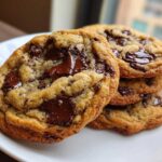 A stack of warm vegan chocolate chip cookies featuring gooey, melted chocolate chunks on a white plate.