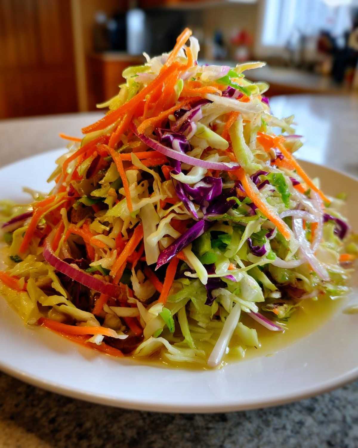 A tall mound of colorful, crunchy cabbage salad featuring shredded green cabbage, purple cabbage, carrots, and red onion.