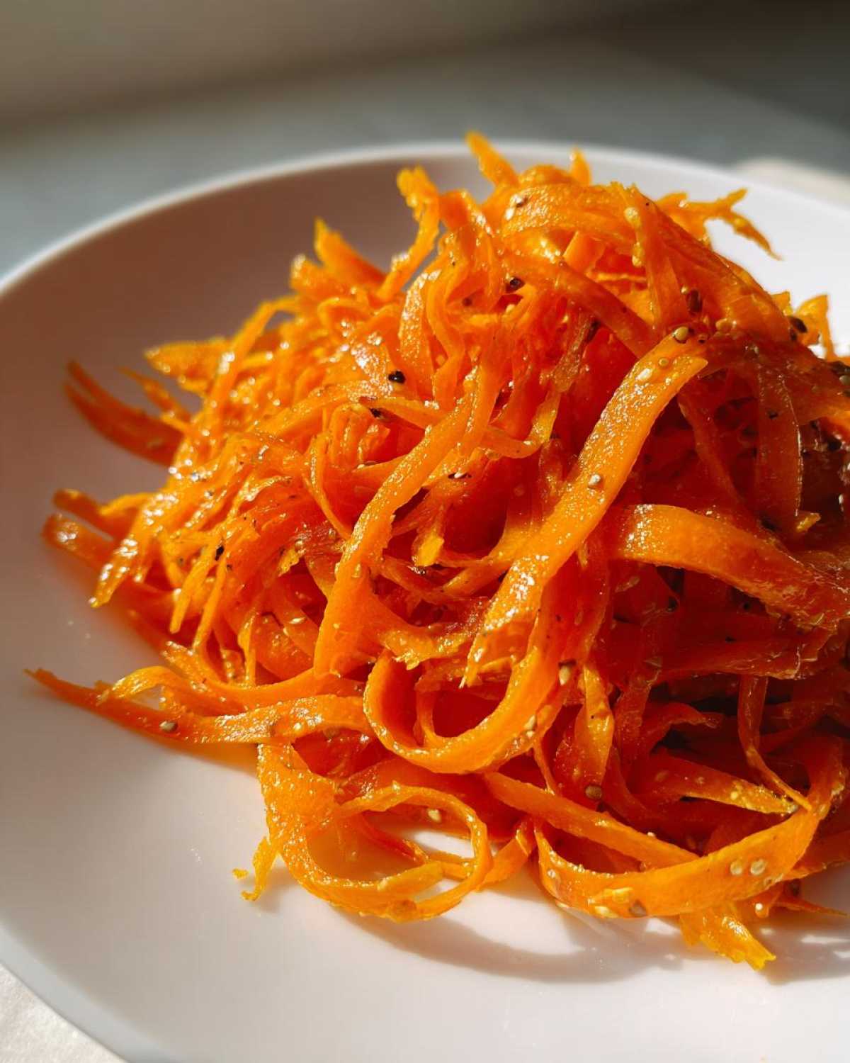 Close-up of bright orange, julienned raw carrot salad seasoned with visible sesame or poppy seeds.