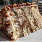 A decadent slice of white German chocolate cake showing layers of white cake, frosting, coconut, and pecans.