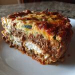 Close-up of a thick, layered slice of zucchini lasagna showing meat sauce, ricotta, and zucchini layers.