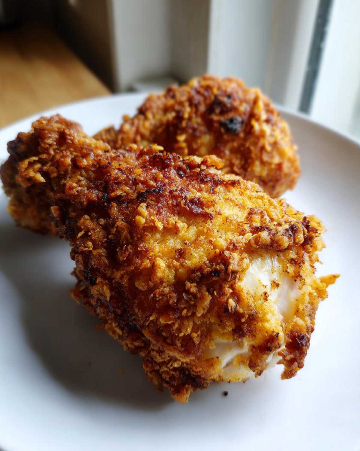 Close-up of two golden-brown, crispy pieces of air fryer fried chicken on a white plate.