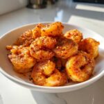A white bowl filled with perfectly cooked, seasoned air fryer frozen shrimp, glowing under natural light.