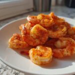A pile of perfectly cooked air fryer frozen shrimp seasoned with paprika and pepper on a white plate.
