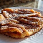 Close-up of freshly fried, golden buñuelos generously coated in cinnamon sugar on a white plate.