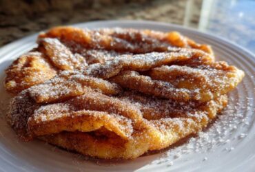 Close-up of freshly fried, golden buñuelos generously coated in cinnamon sugar on a white plate.