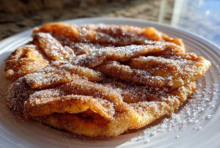 Close-up of freshly fried, golden buñuelos generously coated in cinnamon sugar on a white plate.
