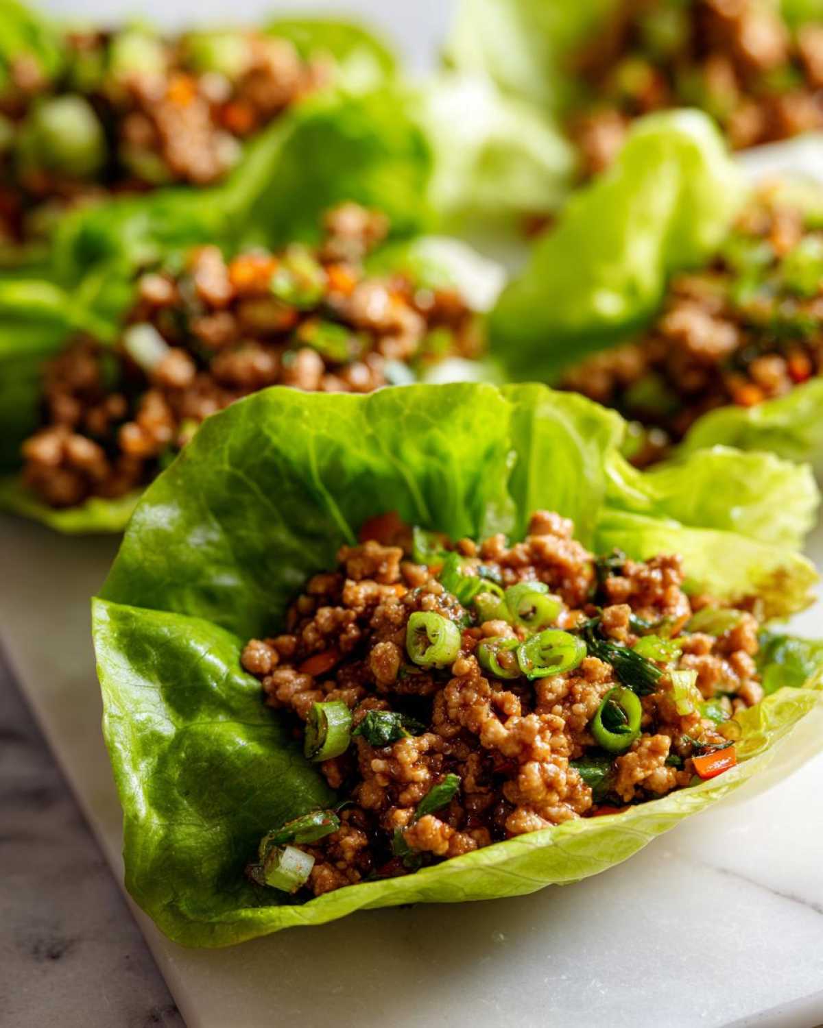 Close-up of a fresh lettuce cup filled with savory ground chicken lettuce wraps mixture, topped with green onions.