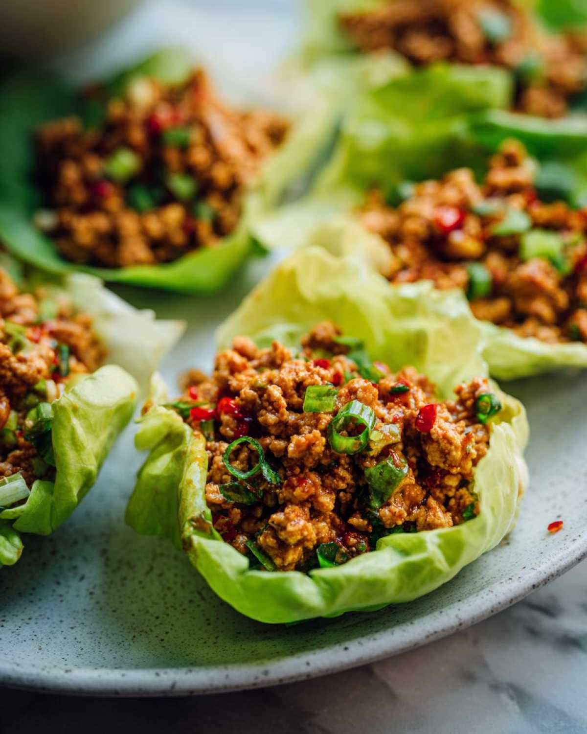 Close-up of several fresh chicken lettuce wraps filled with savory ground chicken mixture and topped with green onions.
