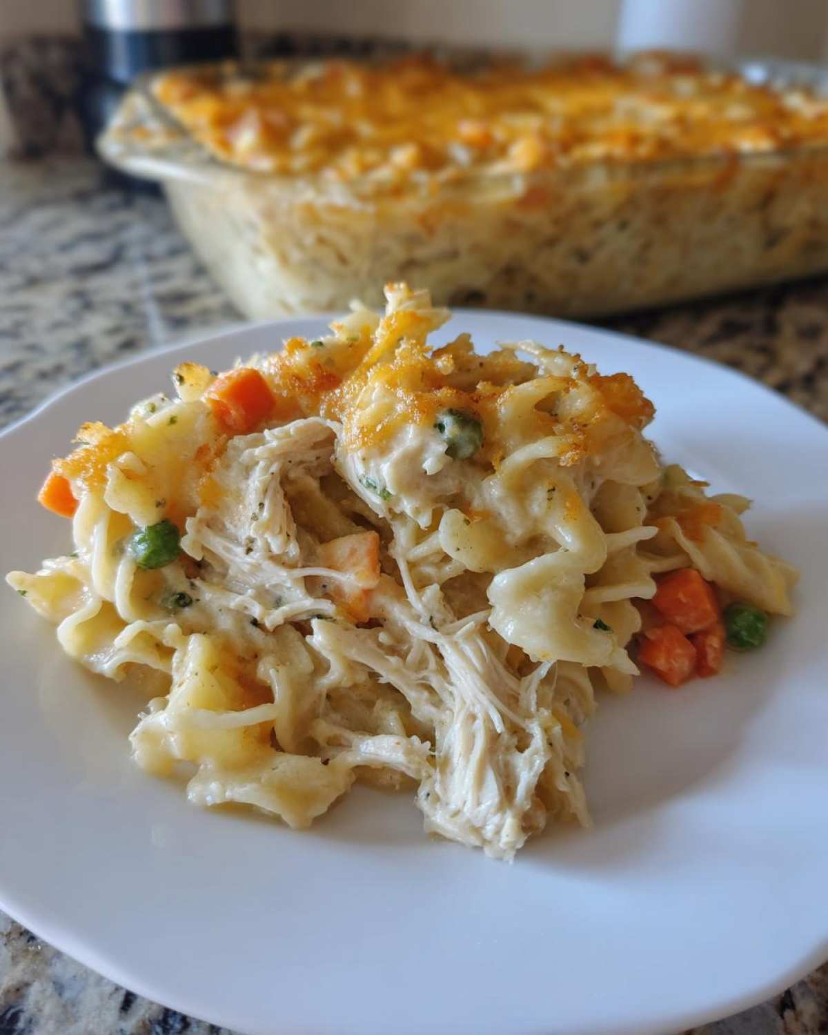 A close-up serving of creamy chicken noodle casserole with shredded chicken, peas, and carrots, topped with melted cheese.