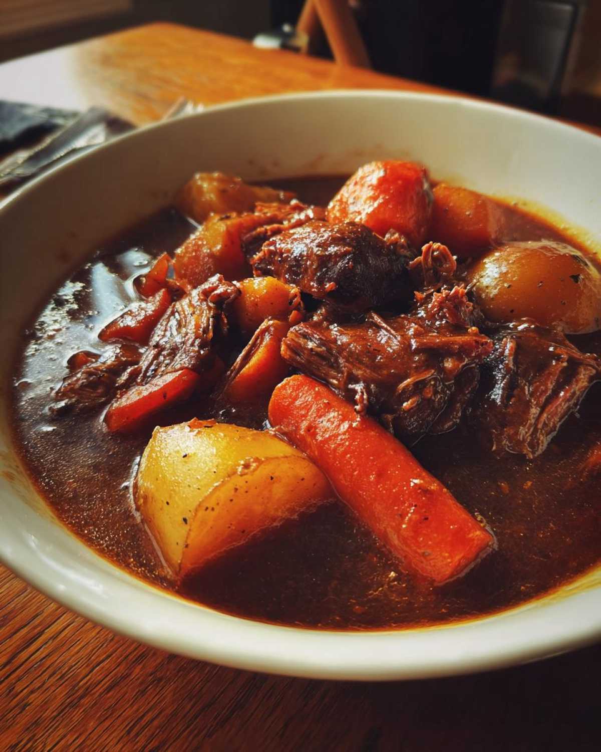 Close-up of a rich, dark bowl of slow-cooked pork stew featuring tender meat, carrots, and potatoes.