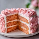 A slice removed from a beautiful pink rose cake, revealing three layers of pink sponge and white frosting layers.