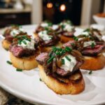 Close-up of several perfectly prepared steak crostini topped with medium-rare steak, creamy cheese, caramelized onions, and chives.