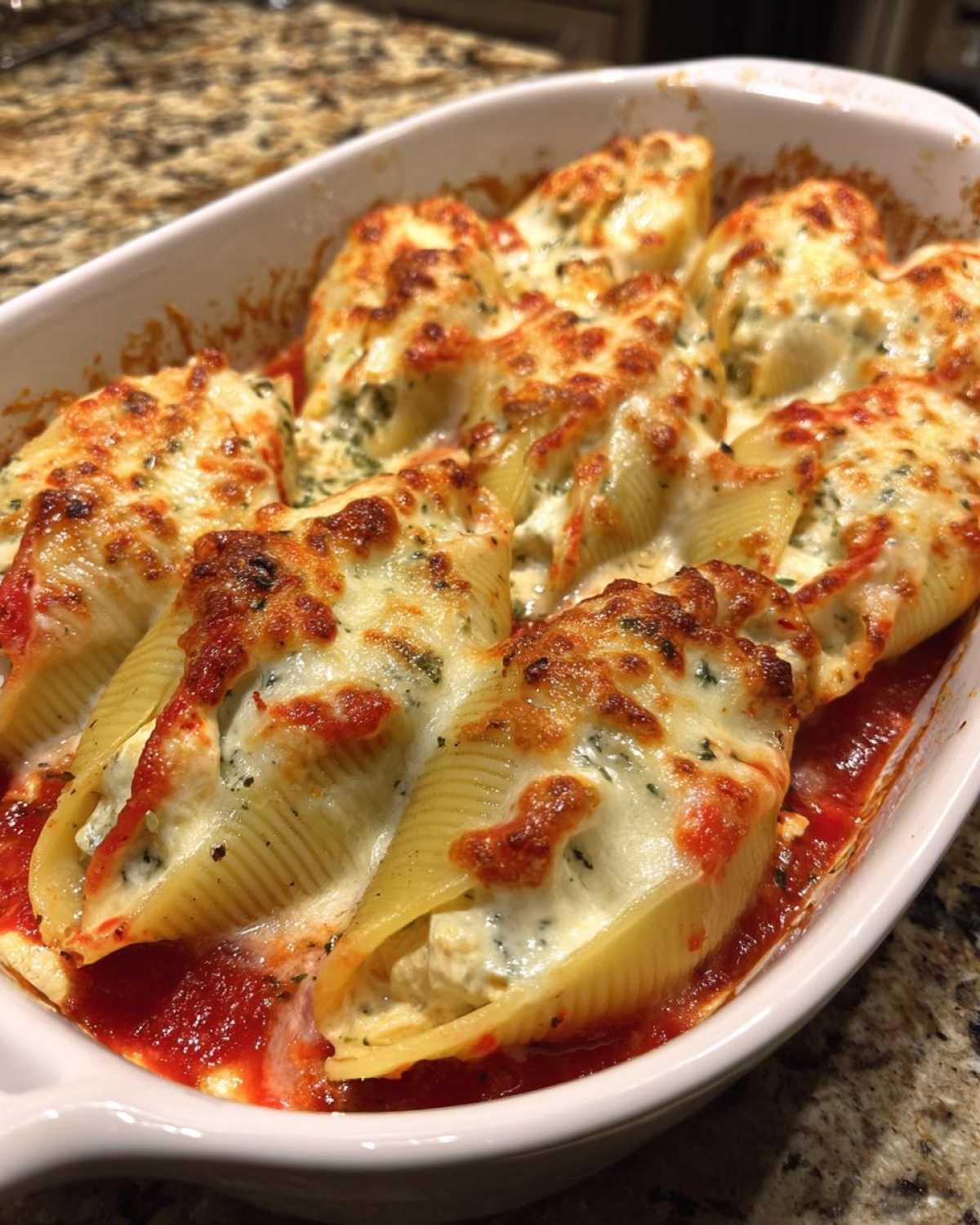 Close-up of baked chicken alfredo stuffed shells topped with browned, melted mozzarella cheese in a white baking dish.