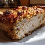 Close-up of a thick slice of baked ranch chicken showing the moist white meat and a golden, crispy, seasoned crust.