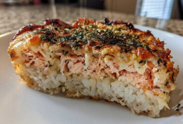A thick slice of baked salmon sushi bake showing layers of white rice, pink salmon filling, and a browned, seasoned topping.