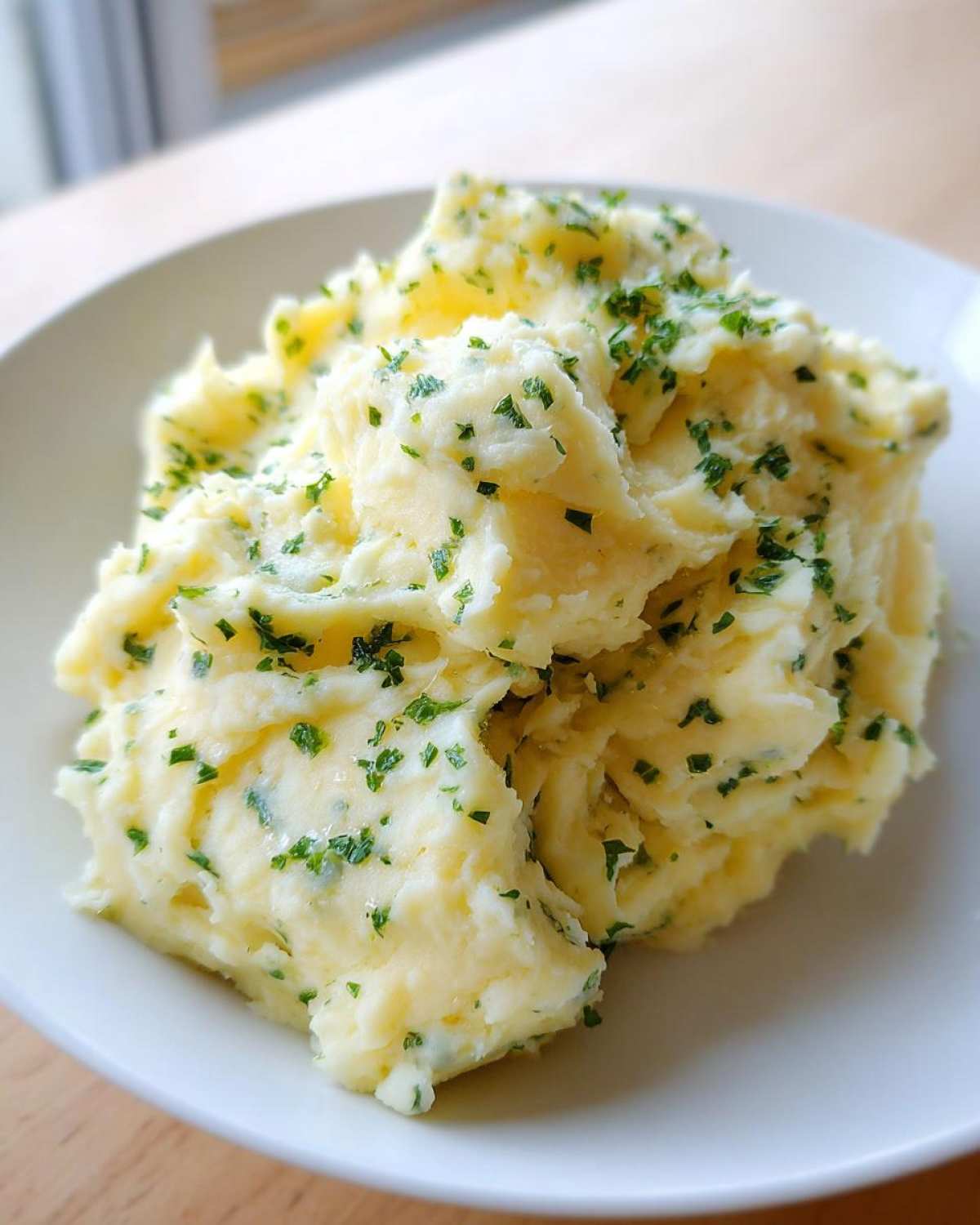 A close-up of creamy, fluffy boursin mashed potatoes topped generously with chopped fresh parsley.