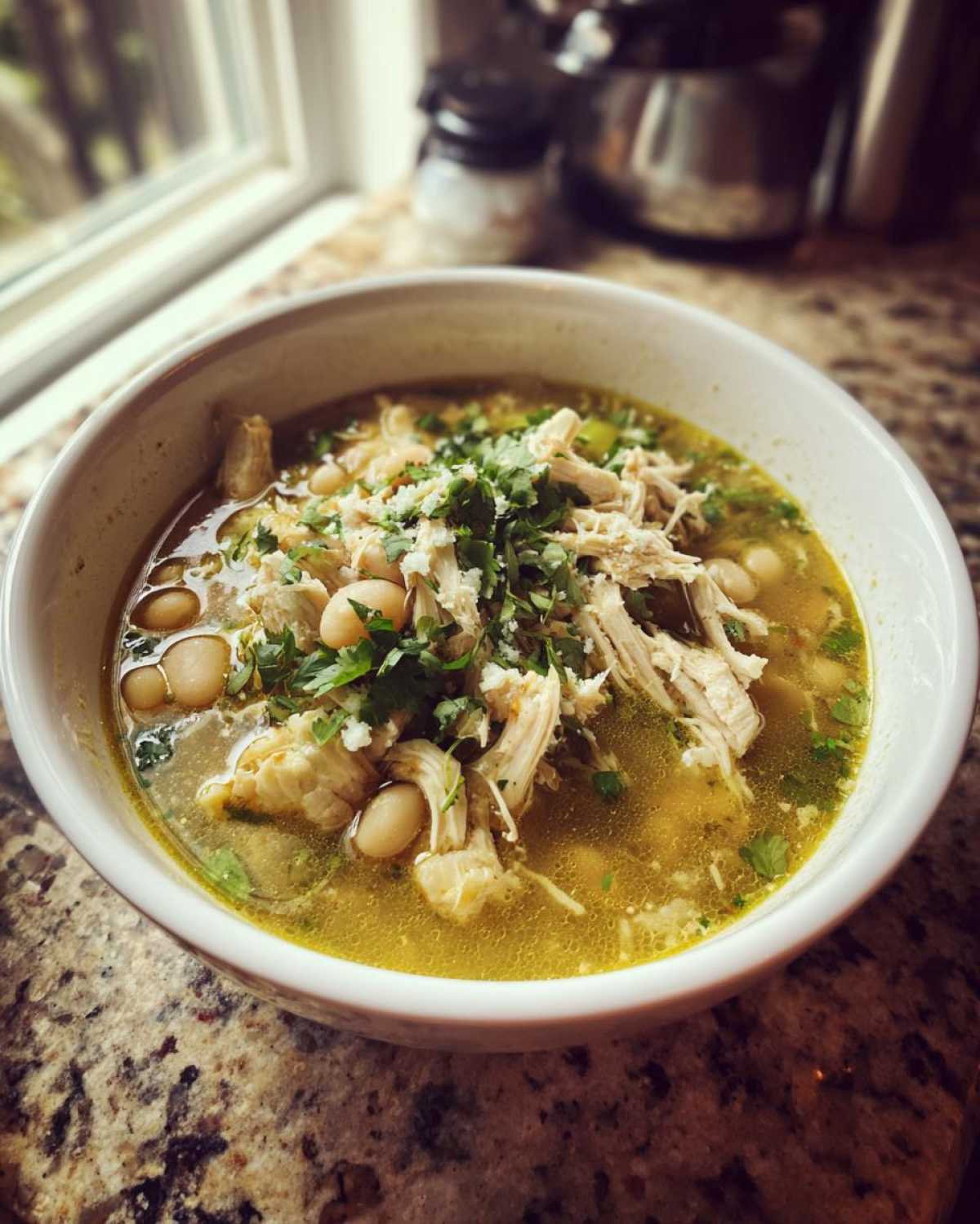 A close-up of a white bowl filled with flavorful chicken pozole, featuring shredded chicken, hominy, and fresh cilantro.
