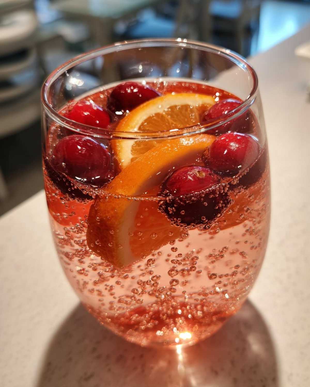 Close-up of a glass filled with bubbling pink champagne punch, garnished with fresh cranberries and an orange slice.
