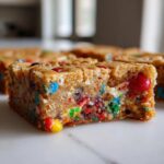 A close-up, cross-section view of a thick, chewy christmas cookie bars loaded with colorful candy pieces.