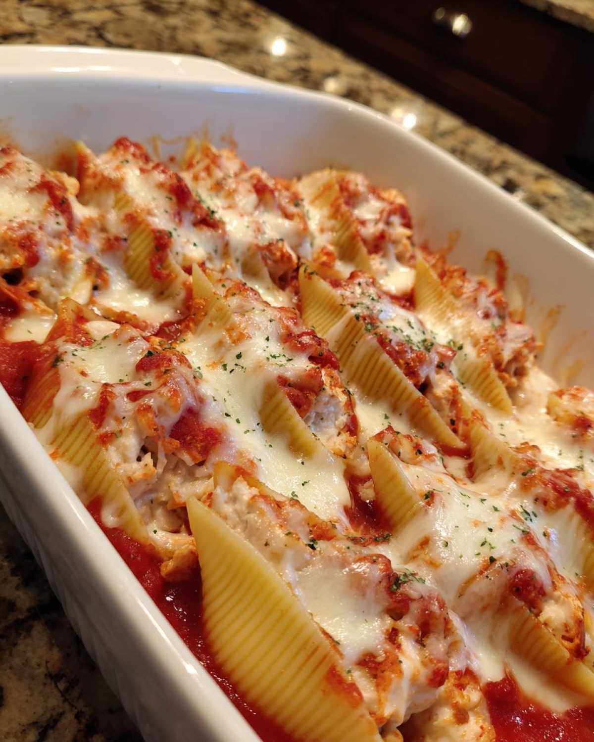 Close-up of baked chicken alfredo stuffed shells topped with melted mozzarella and marinara sauce.