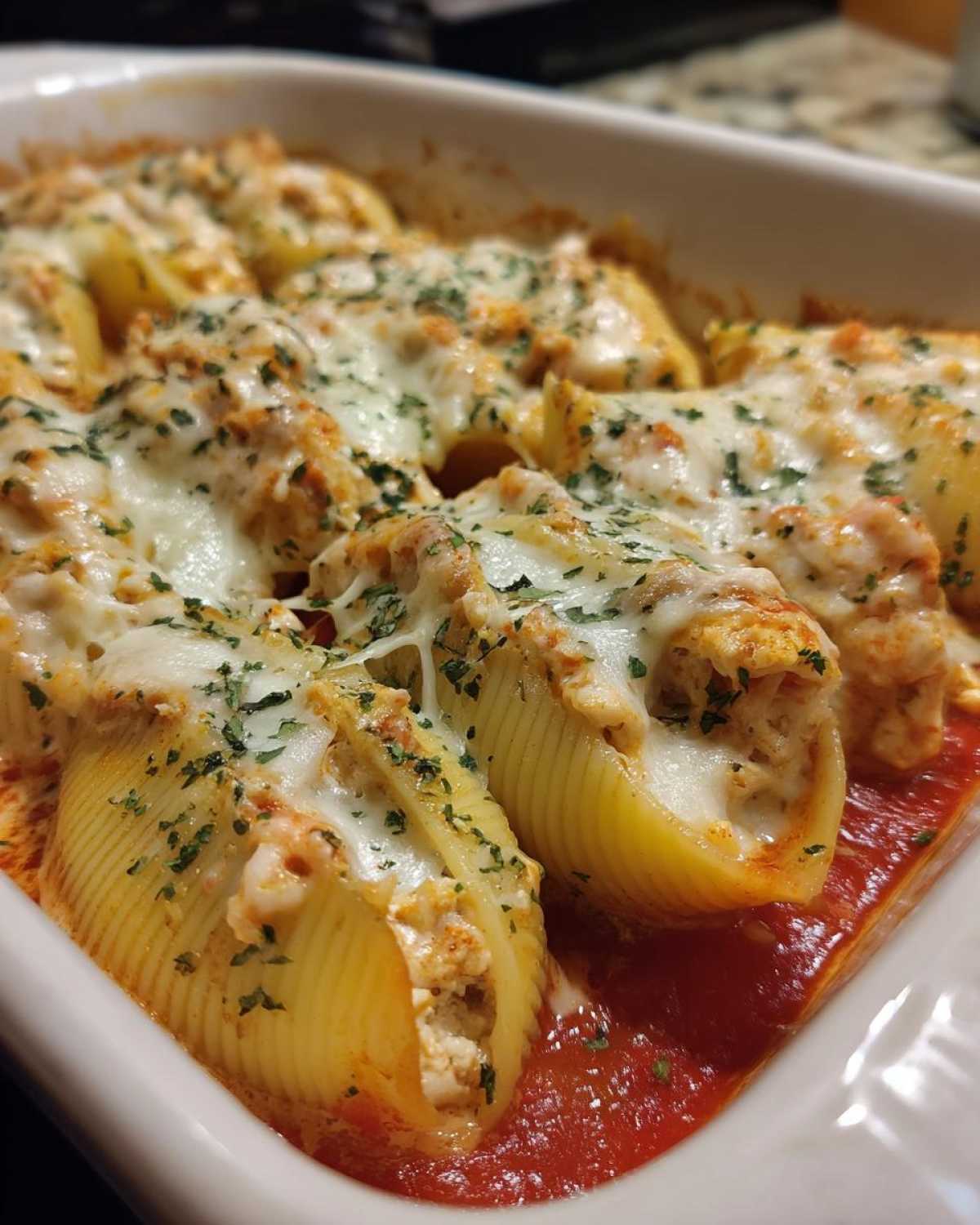 Close-up of baked chicken alfredo stuffed shells topped with melted mozzarella and parsley in a baking dish.