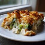 A close-up serving of rich Chicken Divan casserole featuring chunks of chicken, bright green broccoli, and a creamy sauce topped with golden brown crumbs.