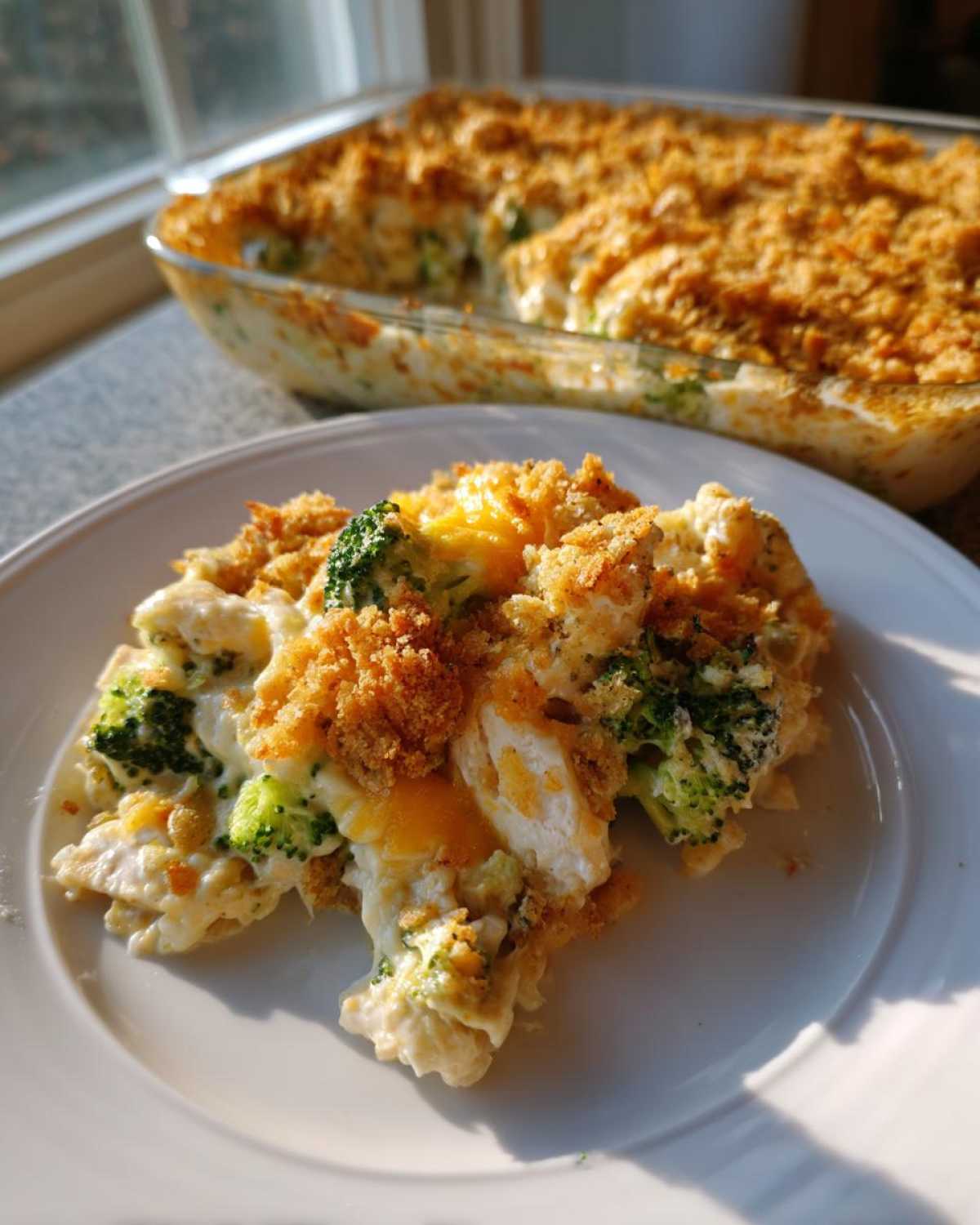 A serving of creamy Chicken Divan casserole featuring chicken, broccoli, and a crunchy breadcrumb topping, with the baking dish in the background.