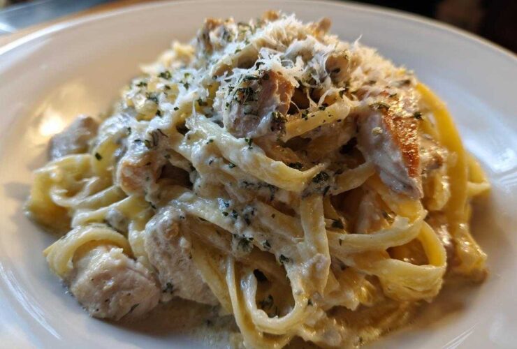 Close-up of a rich serving of chicken fettuccine alfredo, coated in creamy sauce and topped with grated cheese and herbs.