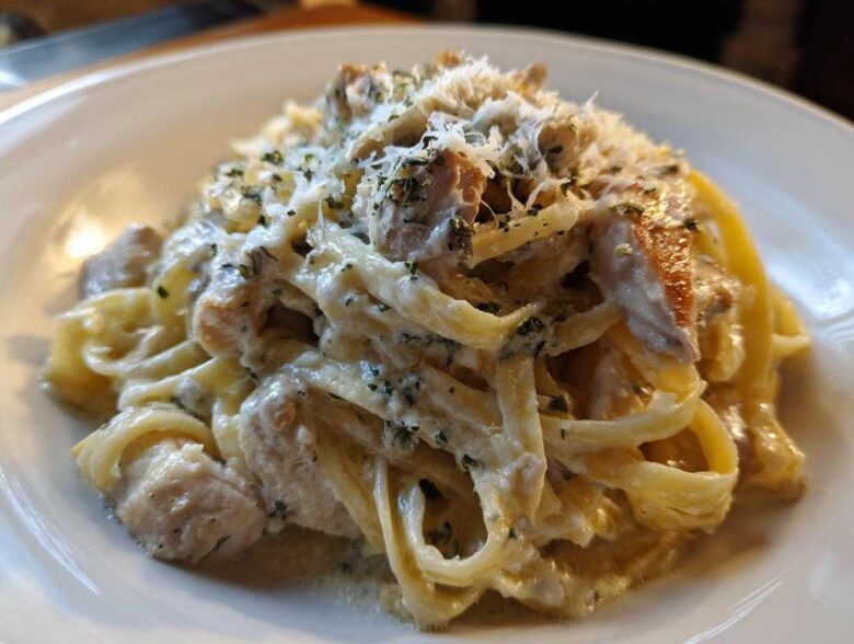 Close-up of a rich serving of chicken fettuccine alfredo, coated in creamy sauce and topped with grated cheese and herbs.