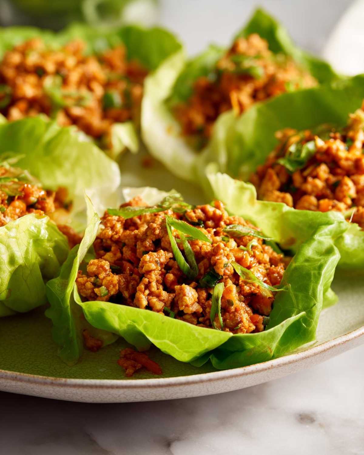 Several servings of savory chicken lettuce wraps filled with seasoned ground chicken and topped with green onions.