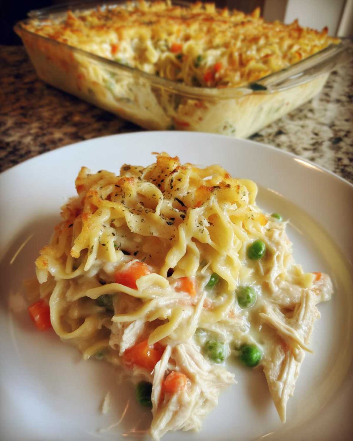 A close-up serving of creamy chicken noodle casserole with peas and carrots, topped with crispy noodles.