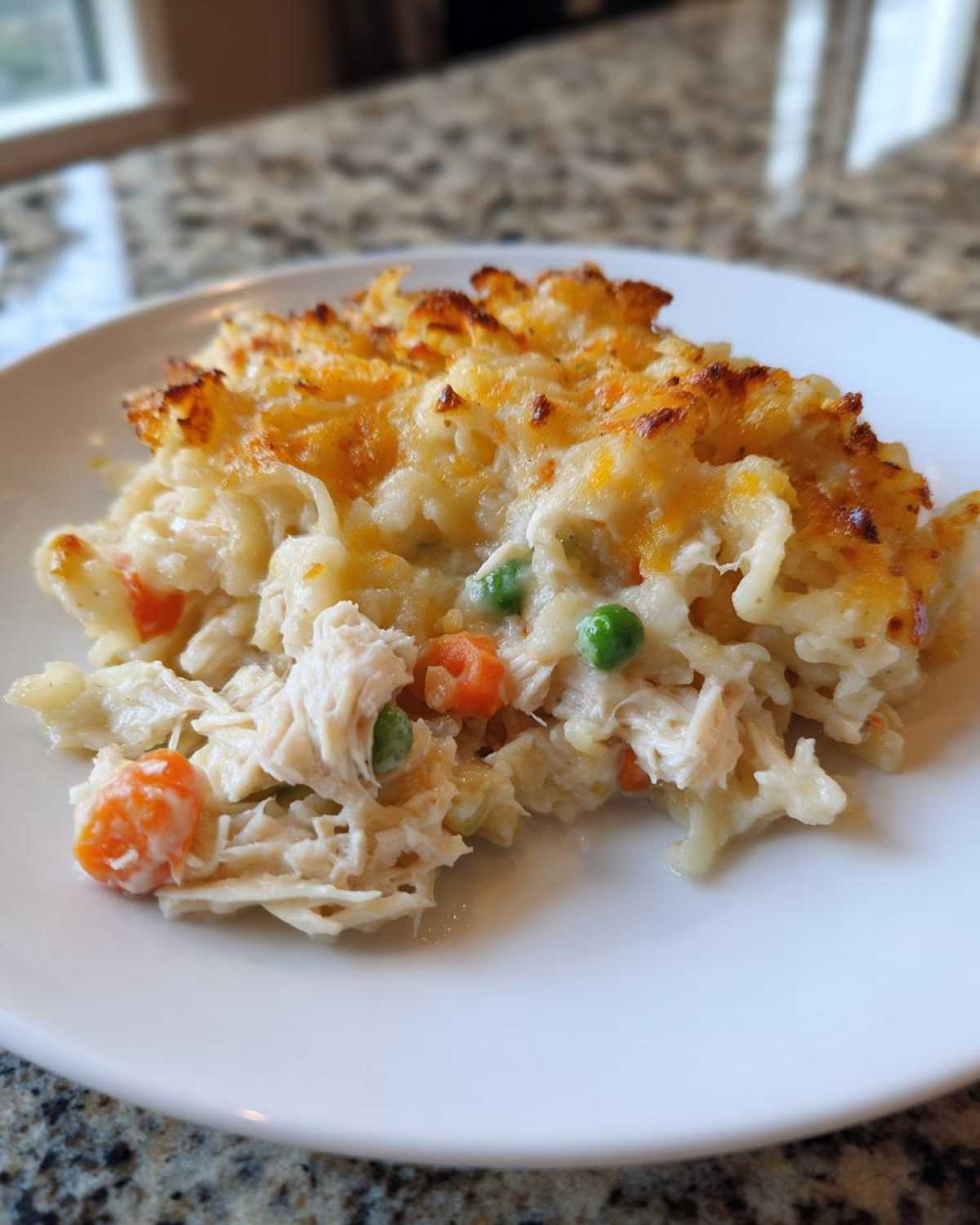 A scoop of creamy chicken noodle casserole with shredded chicken, peas, and carrots, topped with golden melted cheese.