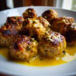 Close-up of several browned chicken piccata meatballs smothered in a bright yellow lemon-caper sauce.