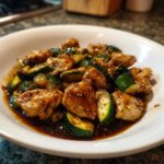 A close-up of juicy chicken pieces and sliced zucchini coated in a rich brown sauce, ready to eat chicken zucchini stir fry.