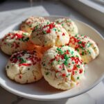 A plate piled high with soft, round christmas sprinkle sugar cookies topped with red and green sprinkles.