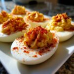 Close-up of several classic deviled eggs, featuring piped yolk filling and a dusting of bright red paprika.