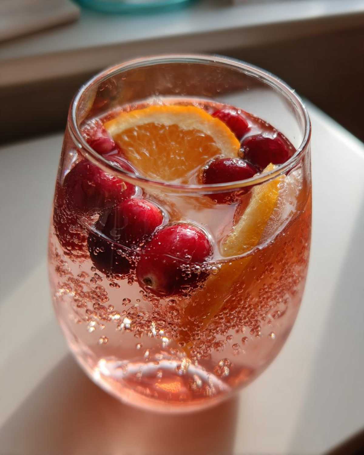 Close-up of a glass filled with pink champagne punch, garnished with whole cranberries and orange slices.