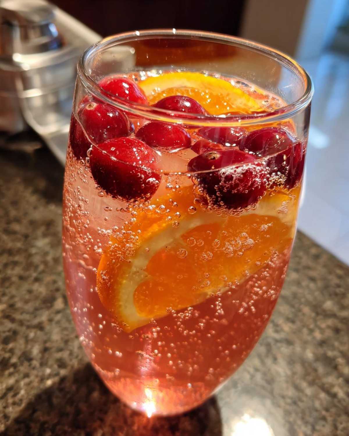 Close-up of a bubbly, pink champagne punch garnished with fresh cranberries and an orange slice.