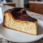 A thick slice of creamy Basque cheesecake featuring a signature dark, caramelized top, served on a white plate.