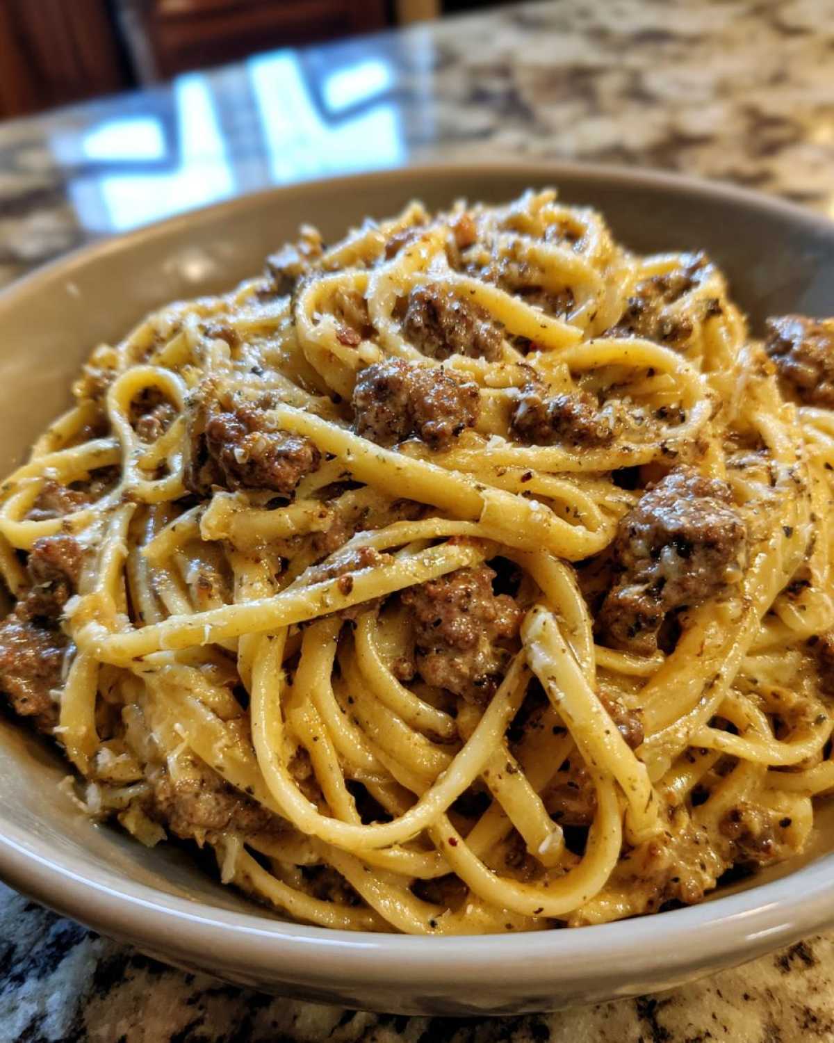 Close-up of a bowl filled with creamy beef pasta, featuring linguine coated in a rich sauce and chunks of seasoned ground beef.